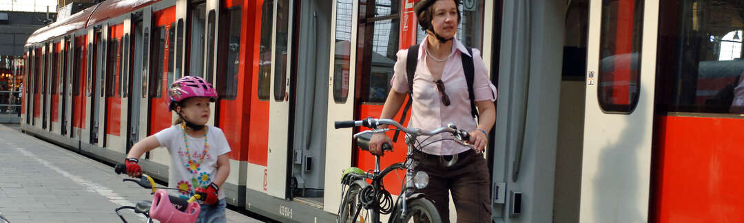 Frau und Mädchen schieben ihre Fahrräder am Bahnsteig neben Zug mit geöffneten Türen