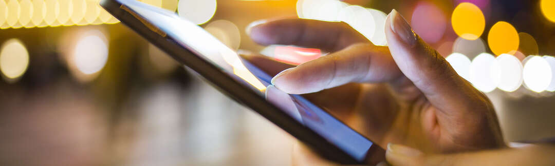 Hände die ein Smartphone bedienen draußen bei Nacht