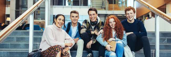 Fünf Schülerinnen und Schüler sitzen in einem Gebäude auf Treppenstufen