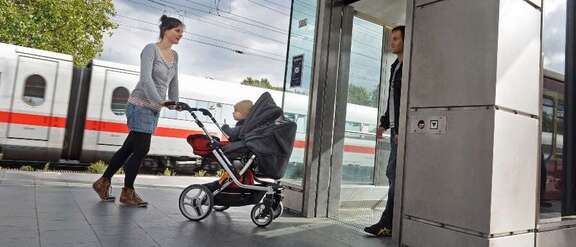 Frau mit Kinderwagen auf Bahnsteig steigt in einen Aufzug