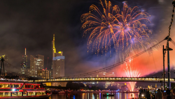 Museumsuferfest Feuerwerk vor der Frankfurter Skyline, Menschen stehen auf dem Holbeinsteg, ein Schiff ist auf dem Main unterwegs