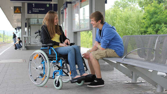 Junges Mädchen im Rollstuhl am Bahngleis mit einem männlichen Begleiter