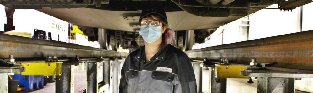 Kira Keller in der vlexx-Werkstatt Frau in Arbeitsklamotten in der Arbeitsgruppe unter einem Zug