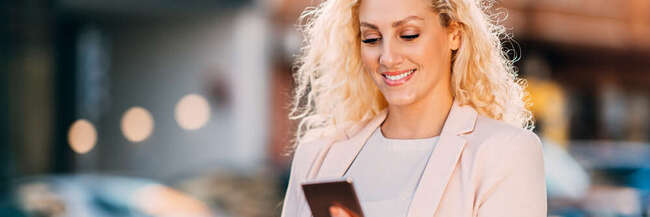Smiling blond woman on the street looking on her mobile phone