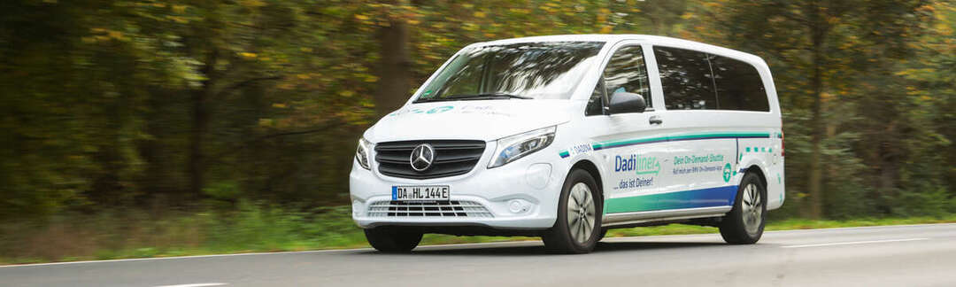 DadiLiner Ein weißes großes Auto fährt auf einer Straße im Grünen