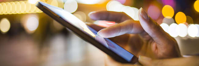 Hände die ein Smartphone bedienen draußen bei Nacht