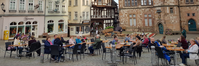 Marburg mehrere Menschen an Tischen sitzend auf gepflastertem Platz vor historischem Steinhaus