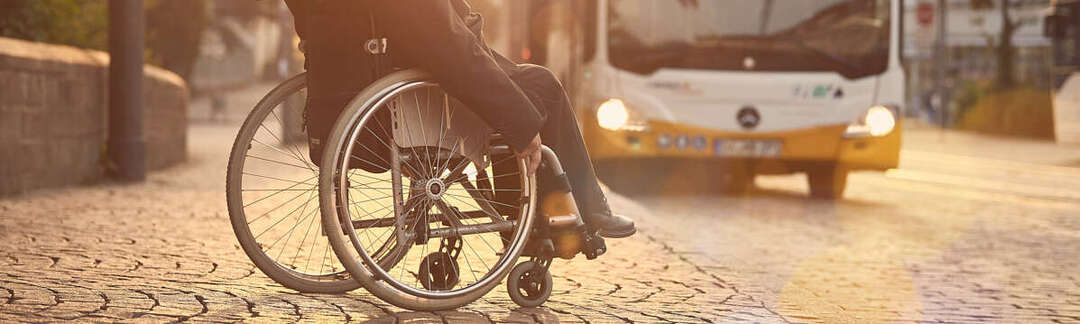 Rollstuhlfahrer blickt auf einen herannahenden Bus