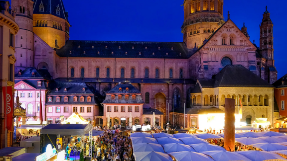 Blick von oben auf den Markt, der mit Menschen gefüllt ist, die unter weißen Schirmen sitzen. Links steht eine Bühne, im Hintergrund ist der Dom.