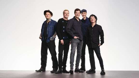 Die Toten Hosen in Frankfurt Die Mitglieder der Toten Hosen stehen dunkel bekleidet zusammen vor weißem Hintergrund und lächeln