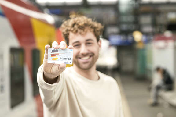 D-Ticket Lachender Mann hält Deutschland-Ticket in die Kamera