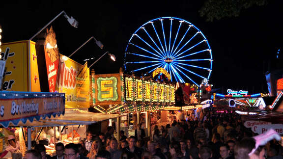 Straße mit Buden und vielen Besuchern auf dem Prämienmarkt mit Riesenrad bei Nacht