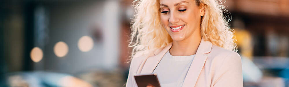 lächelnde Frau auf der Straße mit Smartphone und Coffe-to-go-Becher in der Hand